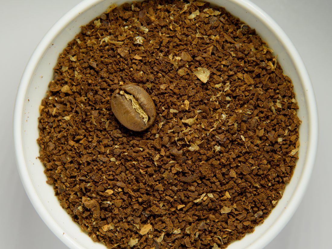 Ground coffee in a white bowl with roasted beans